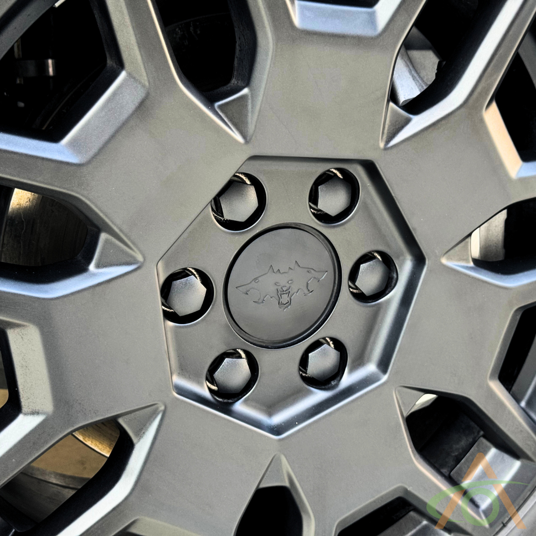 A close-up of a black car wheel rim highlights the Abstract Ocean Cybertruck Wheel Center Caps & Lug Nut Covers, featuring a hexagonal center design and stylish center caps with a logo of a mountain and bull.