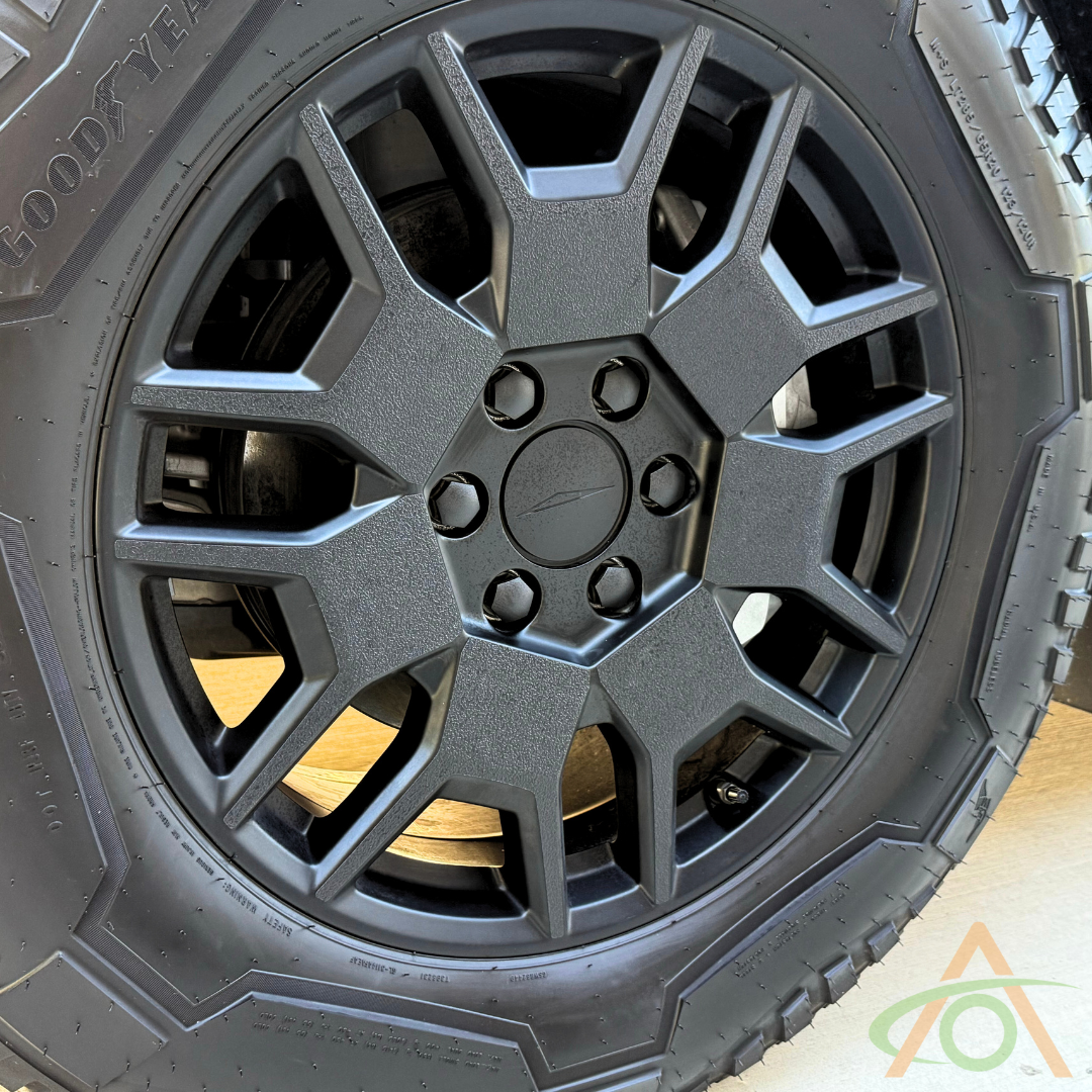A black, multi-spoke wheel with the Xpel Armor All-Terrain Wheel Decals for Cybertruck by Abstract Ocean highlights all-terrain prowess with a visible Goodyear tire.
