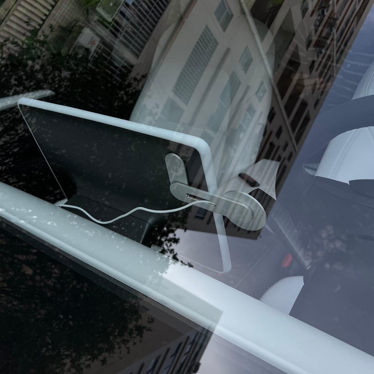 Photo taken through a car window shows a steering wheel and Tesery Official Store's Wireless Magsafe Mount for Tesla Model 3/Y/S/X/Cybertruck with a tablet attached to the dashboard, reflected buildings visible on the glass.