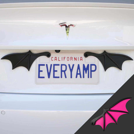 The license plate on a white Tesla showcases EveryAmps decorative black bat wings made from recycled PETG plastic, accompanied by an inset image featuring the magenta version of the License Plate Bat Wings.