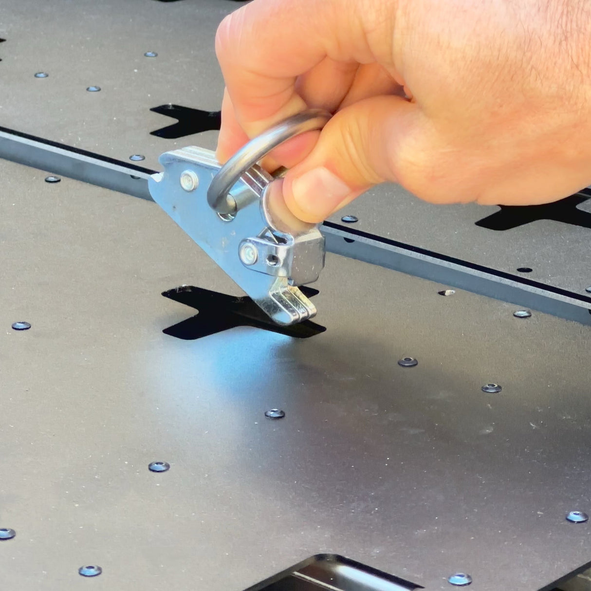 A hand uses a metal tool to lift a precisely cut section from a black metal sheet, ideal for crafting Thunderbolt Adventure Supply’s R1T Bed Glider and innovative truck bed storage camping accessories.