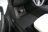 Close-up of the driver-side footwell in a 2026 Tesla Model Y (Juniper) featuring LinerX all-weather black floor mats, accelerator and brake pedals, and part of a white seat.