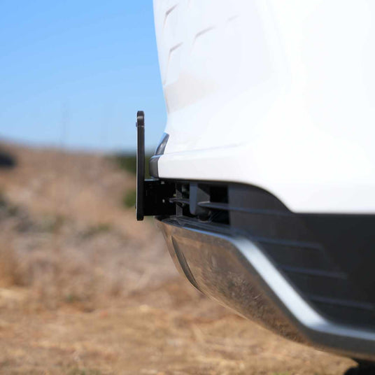 Close-up of a white vehicles rear parking sensor against a blurred outdoor background.