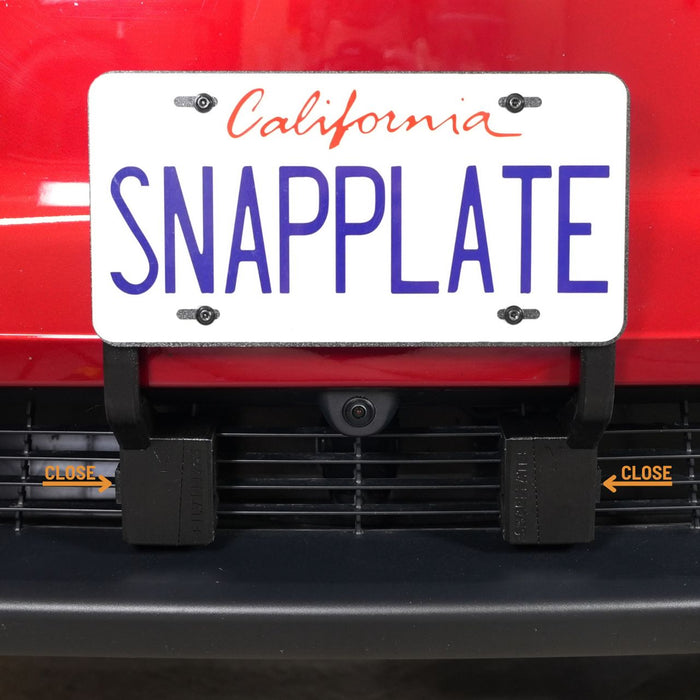 A California license plate reading SNAPPLATE is mounted on a red vehicle using a detachable bracket above a front grill with “CLOSE” labels and arrows.