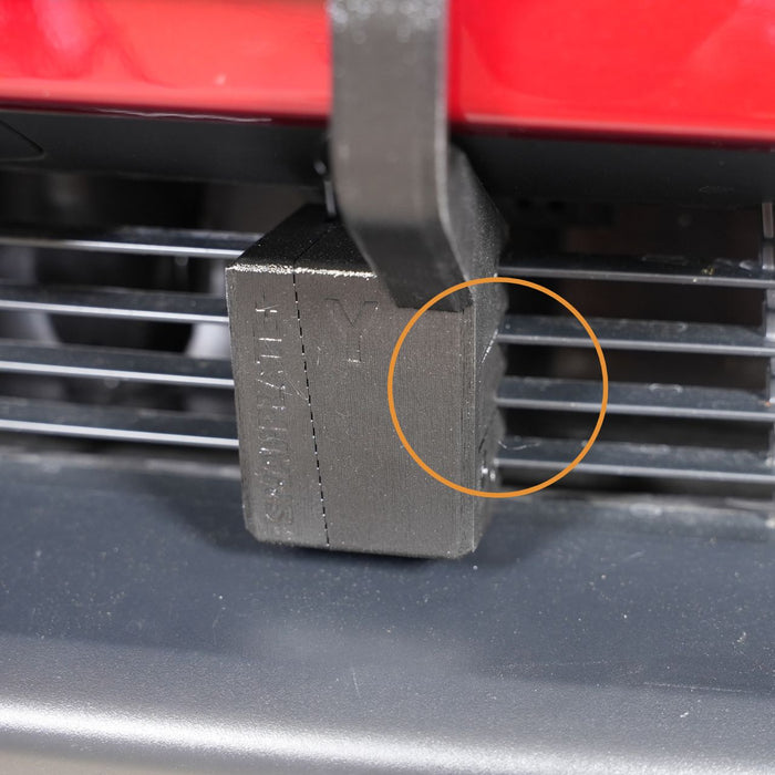 A close-up of a black plastic component attached to horizontal grill slats, with an orange circle highlighting a section on the right side.
