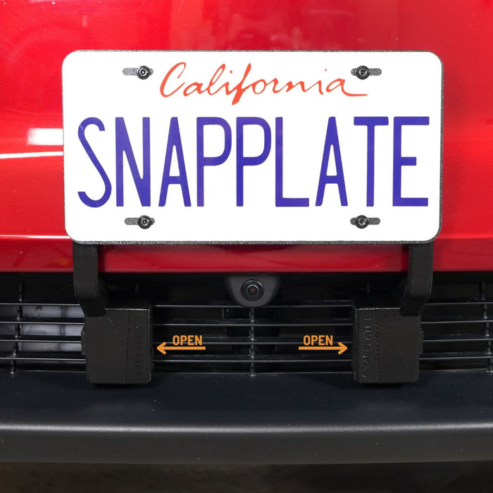 A California license plate reading SNAPPLATE is mounted on a red vehicle using a removable front plate bracket labeled OPEN with arrows pointing outward.