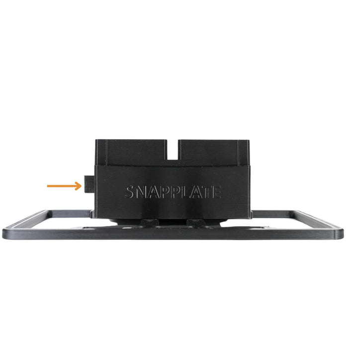 Black plastic mount labeled SNAPPLATE attached to a license plate frame, with an arrow pointing to a small tab on the left side.