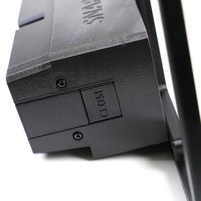 Close-up of a black plastic device with a sliding switch labeled CLOSE and visible screws on its surface.