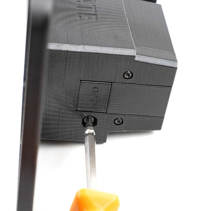 A screwdriver is inserted into a screw on a black plastic device, near a labeled panel that reads RESET.
