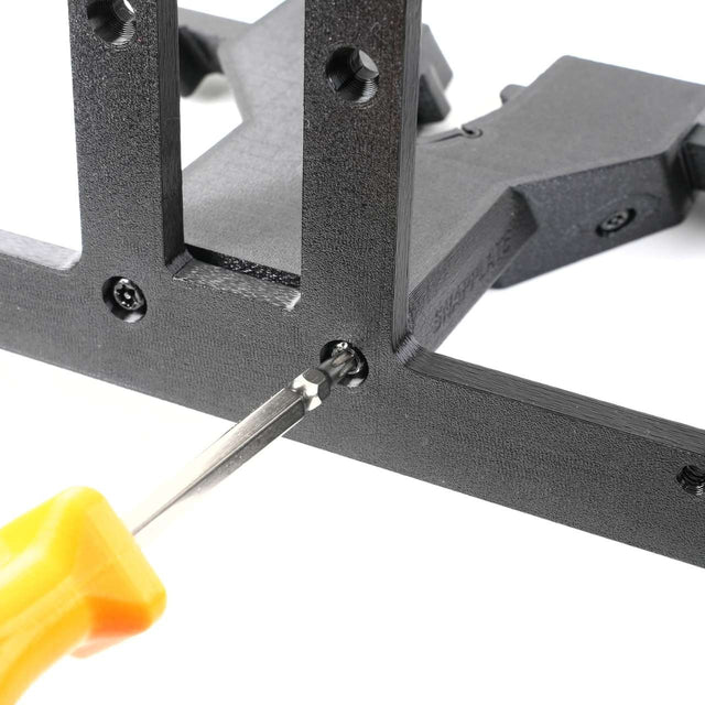 A close-up of a screwdriver with a yellow handle tightening a screw on a black plastic frame.