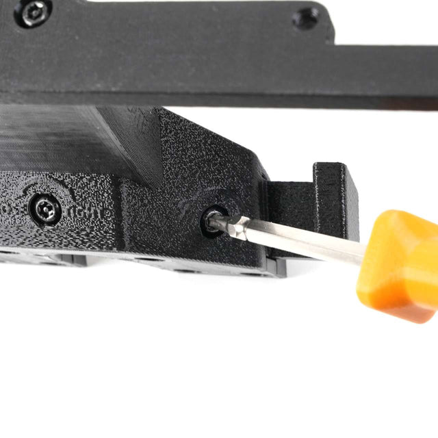 A close-up of a screwdriver with a yellow handle tightening a screw into a black plastic or metal component.