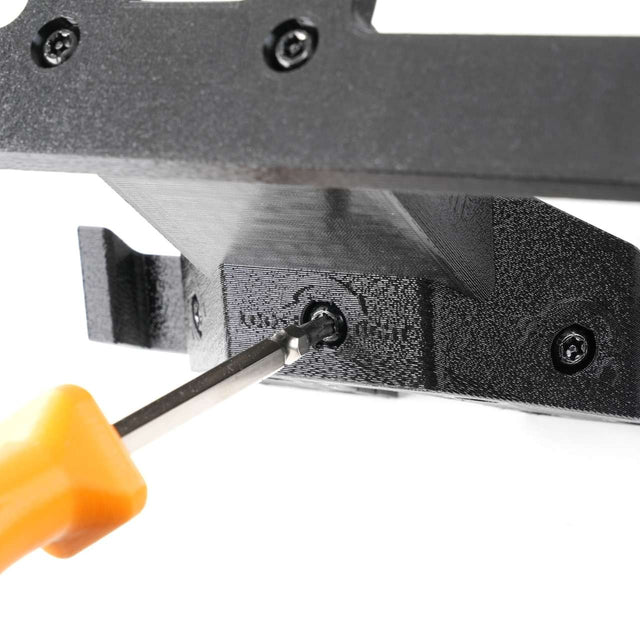 A screwdriver with an orange handle is tightening a screw into a black metal or plastic bracket with other visible screws.