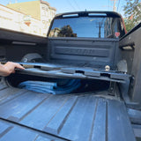 A person lifts the Thunderbolt Adventure Supply R1T Bed Glider in the truck bed, revealing neatly organized blankets and camping accessories stored inside.