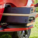 A person slides out the Thunderbolt Adventure Supply Overland Kitchen with updated Gear Sled from the bed of a Rivian R1T pickup, using it as a camping kitchen on grassy ground.
