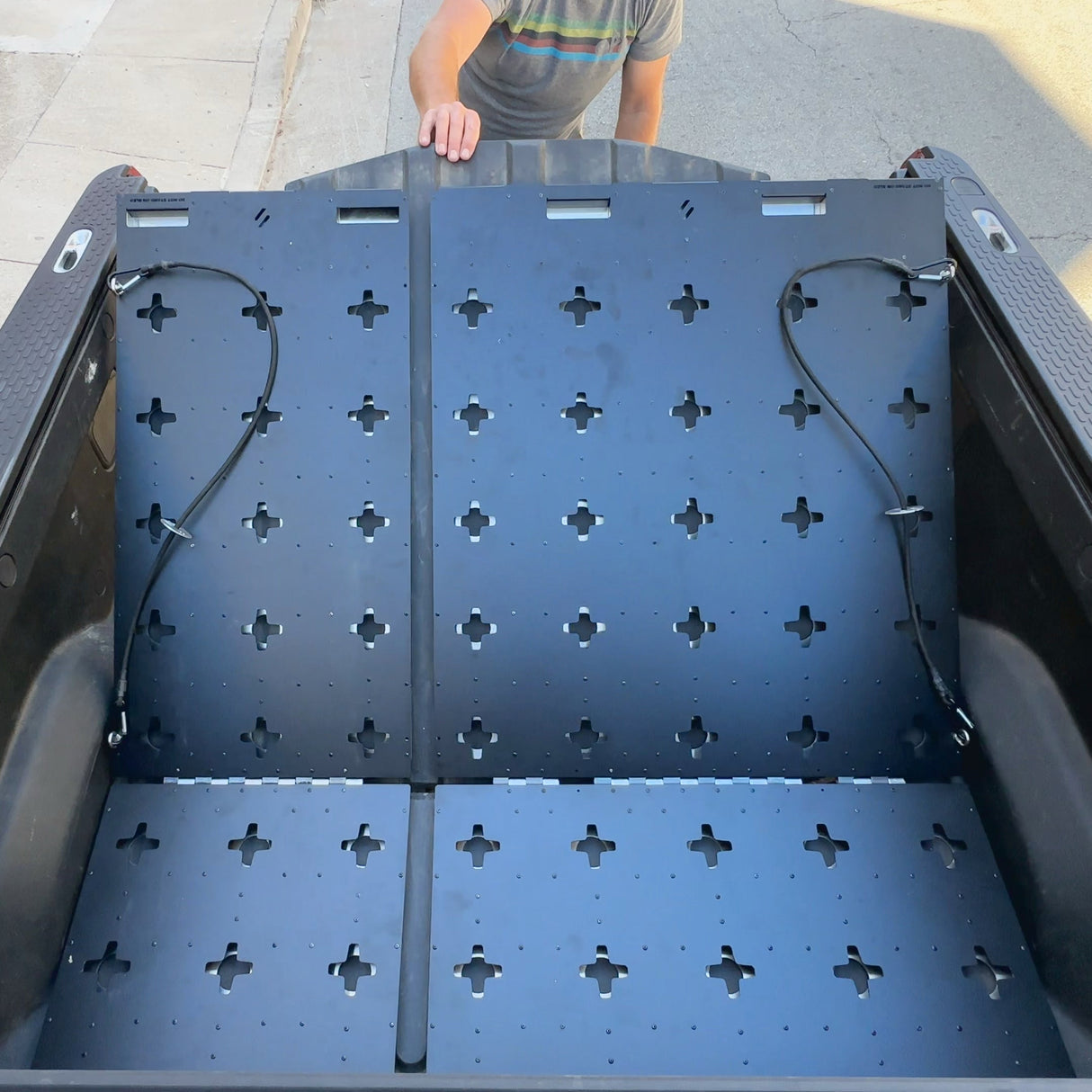 A person stands behind a pickup truck with Thunderbolt Adventure Supply’s R1T Bed Glider and modular metal panel system installed in the bed.