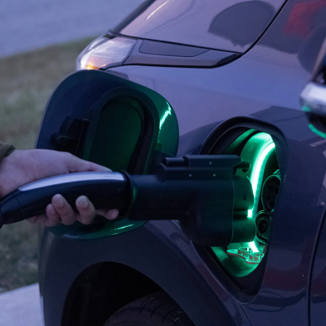 A person uses the A2Z NACS Charger to CCS1 Vehicle Adapter to plug a charging cable into an electric vehicle's port, illuminated with green light, enabling seamless DC fast charging.