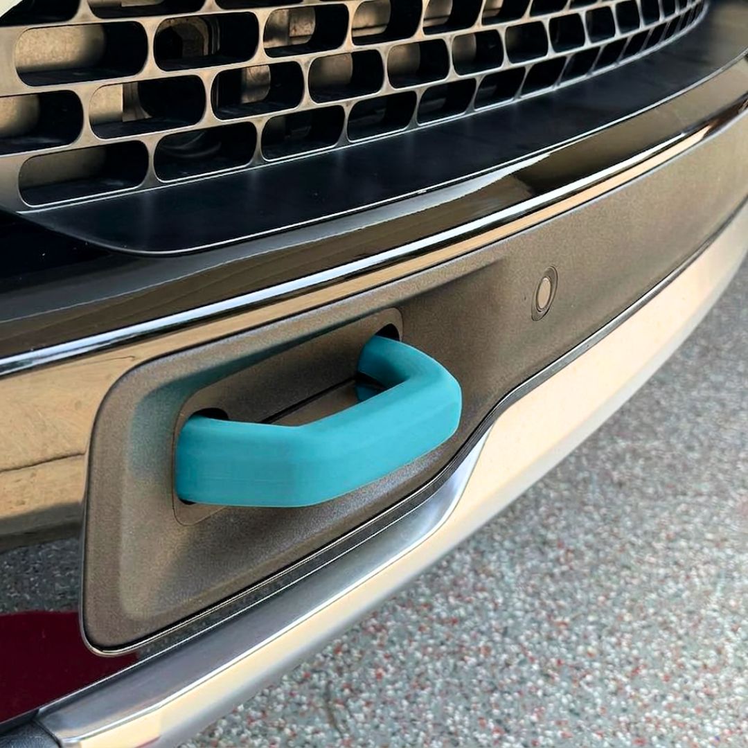 Close-up of a car’s front bumper featuring a teal blue tow hook inserted into a rectangular slot below the grille, with Abstract Ocean Silicone Hook Covers - Pair offering added protection and style.