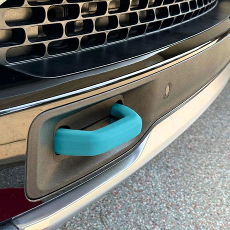 Close-up of a car’s front bumper featuring a teal blue tow hook inserted into a rectangular slot below the grille, with Abstract Ocean Silicone Hook Covers - Pair offering added protection and style.