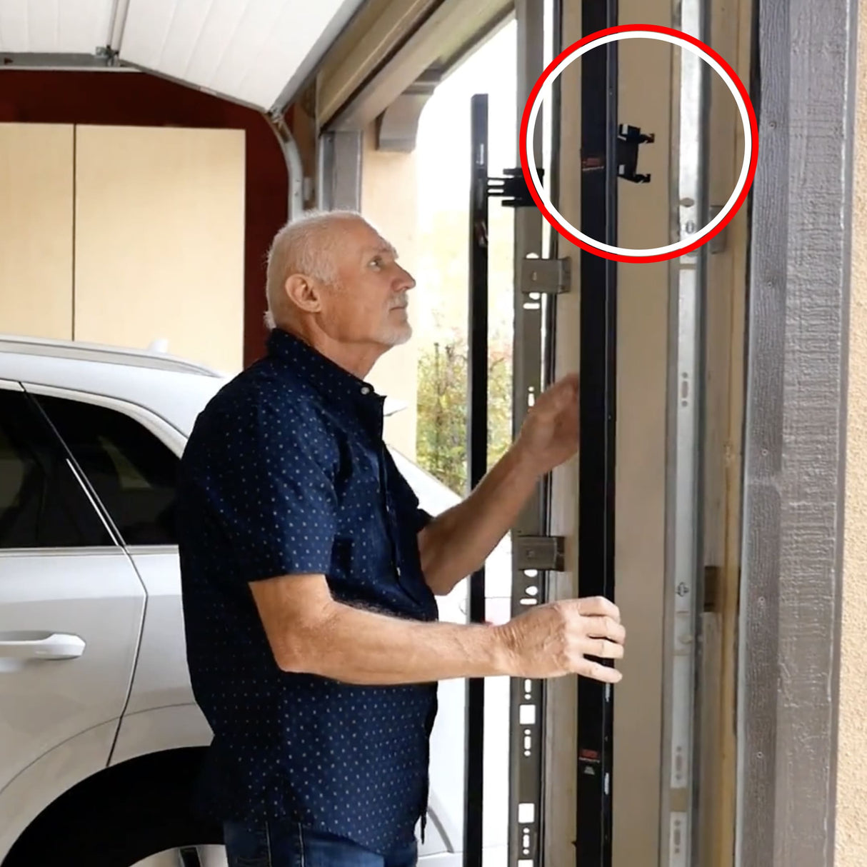 An older man inspects a garage door track in a garage; a red circle highlights The Infinity Shield Infinity Shield Brackets and the garage door sensor mounted on the vertical rail near the top.