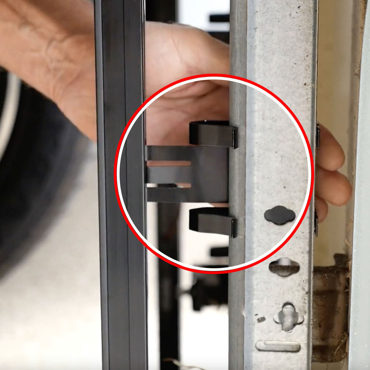 A hand adjusts a black metal latch on a vertical frame, with the latch in a red circle; nearby are The Infinity Shield Infinity Shield Brackets, designed for mounting garage door sensors.